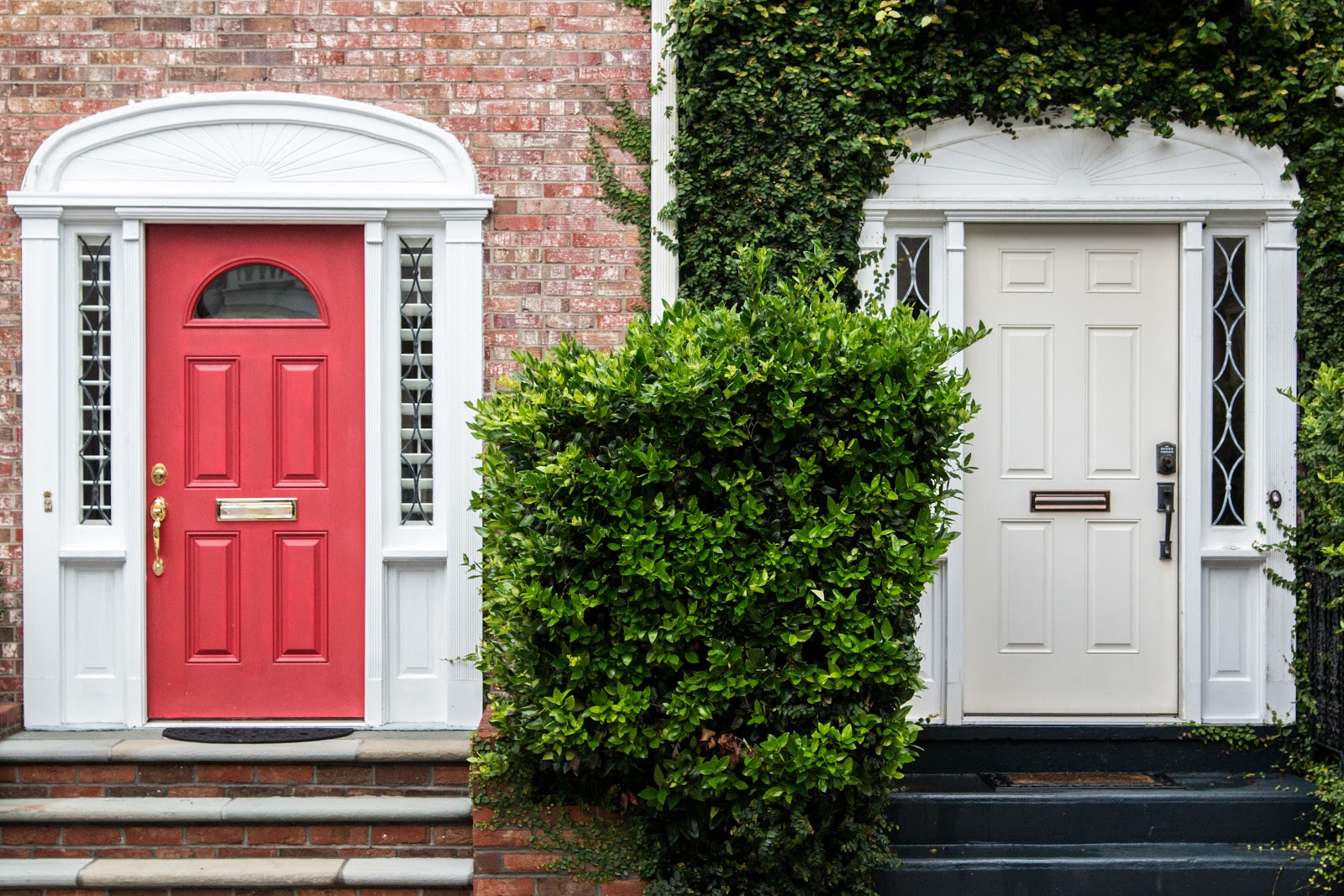 Two front doors, one red to a brick house and one white to a house with greenery