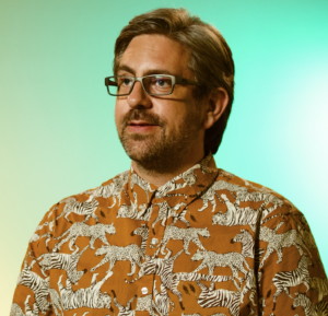 Matthew Robinson in a colorful shirt with tigers and a colroful greenish yellow background to the image